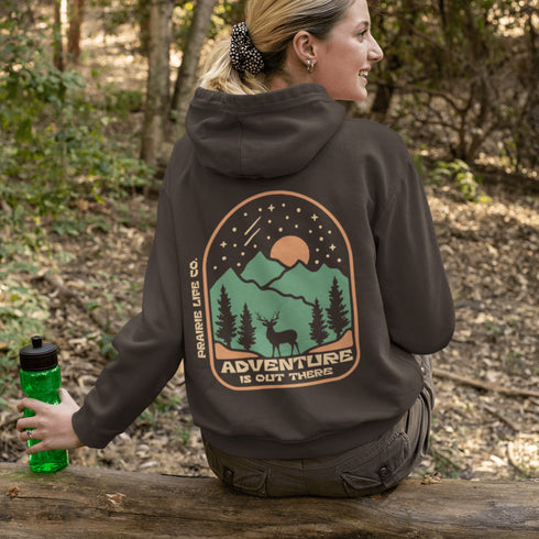This graphic hoodie features a majestic deer standing against a wilderness backdrop— mountains, towering pines, a glowing moon, and a star-filled night sky.