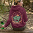 This graphic hoodie features a majestic deer standing against a wilderness backdrop— mountains, towering pines, a glowing moon, and a star-filled night sky.