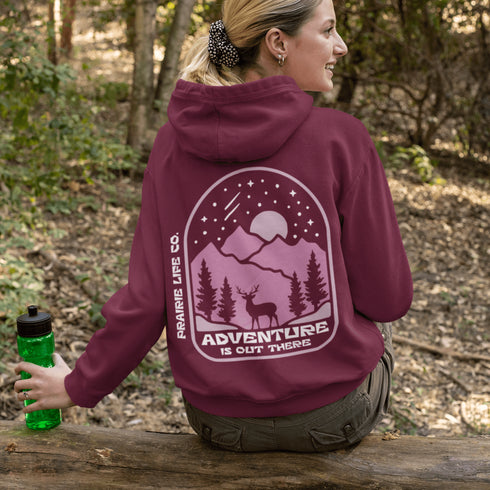 This premium hoodie features a wilderness graphic of a deer under a starry sky, complete with mountains, pine trees, a glowing moon.