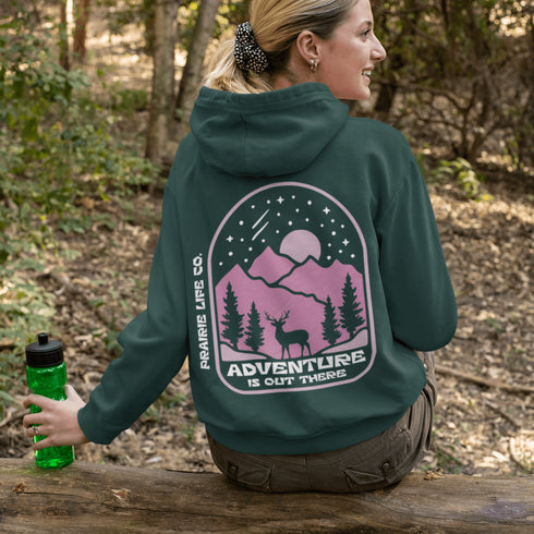 This premium hoodie features a wilderness graphic of a deer under a starry sky, complete with mountains, pine trees, a glowing moon.