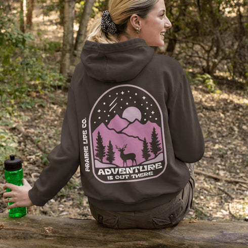 This premium hoodie features a wilderness graphic of a deer under a starry sky, complete with mountains, pine trees, a glowing moon.