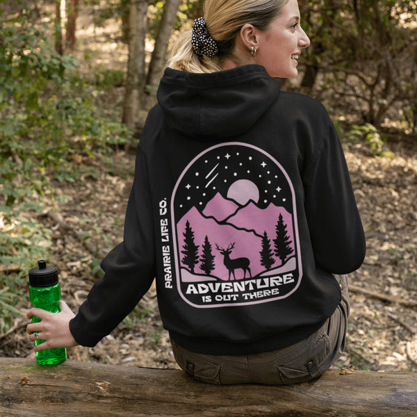 This premium hoodie features a wilderness graphic of a deer under a starry sky, complete with mountains, pine trees, a glowing moon.