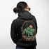 This graphic hoodie features a majestic deer standing against a wilderness backdrop— mountains, towering pines, a glowing moon, and a star-filled night sky.