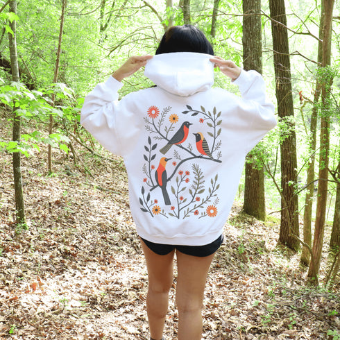 Wrap yourself in the charm of nature with our Among the Leaves Hoodie, a wearable piece of folk art that celebrates the harmony of birds, branches, and blooms.