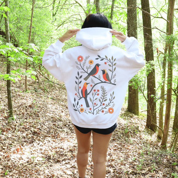 Wrap yourself in the charm of nature with our Among the Leaves Hoodie, a wearable piece of folk art that celebrates the harmony of birds, branches, and blooms.