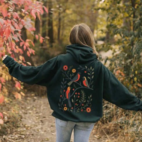 Wrap yourself in the charm of nature with our Among the Leaves Hoodie, a wearable piece of folk art that celebrates the harmony of birds, branches, and blooms.