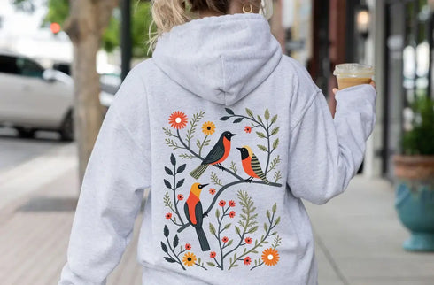 Wrap yourself in the charm of nature with our Among the Leaves Hoodie, a wearable piece of folk art that celebrates the harmony of birds, branches, and blooms.