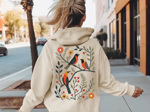 Wrap yourself in the charm of nature with our Among the Leaves Hoodie, a wearable piece of folk art that celebrates the harmony of birds, branches, and blooms.