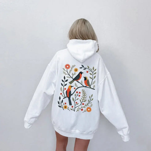 Wrap yourself in the charm of nature with our Among the Leaves Hoodie, a wearable piece of folk art that celebrates the harmony of birds, branches, and blooms.