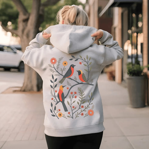 Wrap yourself in the charm of nature with our Among the Leaves Hoodie, a wearable piece of folk art that celebrates the harmony of birds, branches, and blooms.