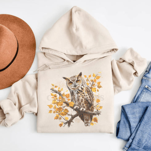 This hoodie features a beautifully detailed owl perched on a branch, surrounded by a scattering of warm-toned autumn leaves.
