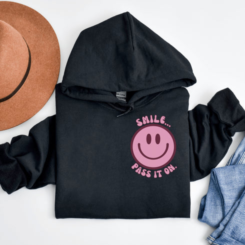 Introducing the latest must-have in your wardrobe that's guaranteed to turn frowns upside down: the Happy Face Hoodie emblazoned with the cheer-spreading command, "Smile...Pass it on." This isn't just any ordinary hoodie; it's your ticket to becoming a walking, talking (and very cozy) ambassador of joy!