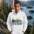 Person wearing a hoodie with a British Columbia design in front of a scenic mountain and lake background