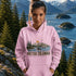 Person wearing a pink hoodie with a British Columbia design, standing in front of a scenic mountain and lake view.