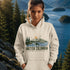 Person wearing a hoodie with a British Columbia design in front of a scenic lake and mountains.