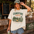 Woman wearing a 'Campfire Nights' t-shirt in a rustic setting with a chalkboard menu.