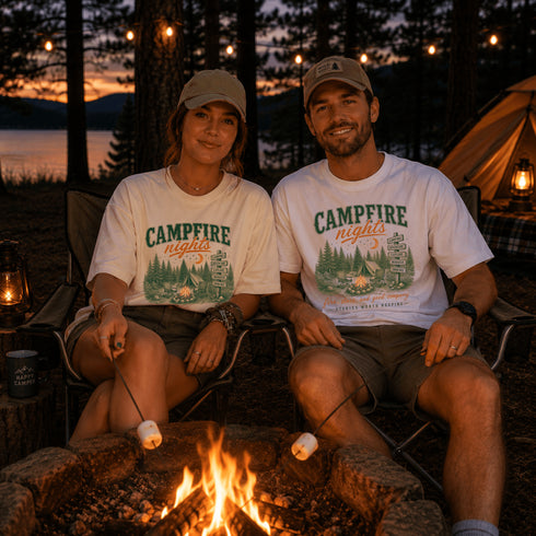 Two people sitting by a campfire wearing 'Campfire Nights' t-shirts with a scenic background.