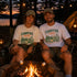 Two people sitting by a campfire wearing 'Campfire Nights' t-shirts with a scenic background.