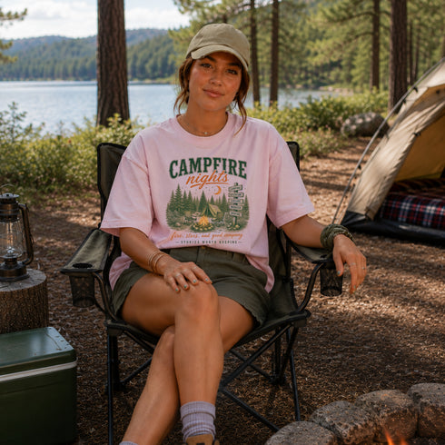 Person sitting in a campsite wearing a 'Campfire Nights' t-shirt with a scenic background.