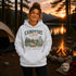 A woman stands outdoors at a campsite at sunset wearing a white pullover hoodie with a large vintage-style camp graphic that reads 'CAMPFIRE nights' and 'Seven Stars and Good Company - Outside North Dakota.' A tent, campfire, lake, mountains, and trees are visible in the background.