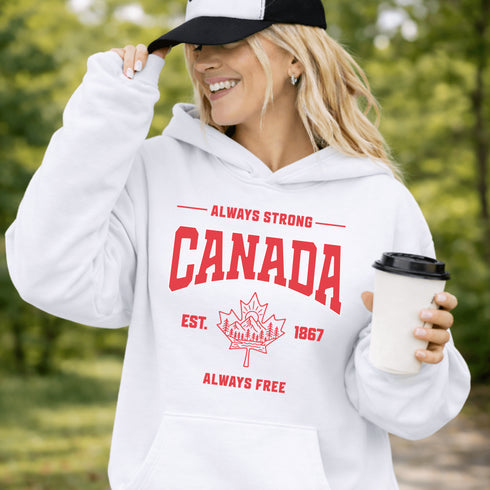 Woman wearing white Canada Always Strong hoodie with red maple leaf graphic and “Est. 1867” design, styled outdoors in a natural setting