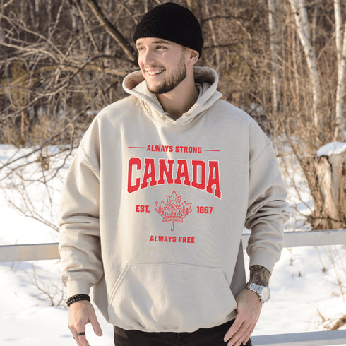 Woman wearing white Canada Always Strong hoodie with red maple leaf graphic and “Est. 1867” design, styled outdoors in a natural setting