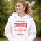 Woman wearing white Canada Always Strong hoodie with red maple leaf graphic and “Est. 1867” design, styled outdoors in a natural setting