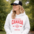 Woman wearing white Canada Always Strong hoodie with red maple leaf graphic and “Est. 1867” design, styled outdoors in a natural setting