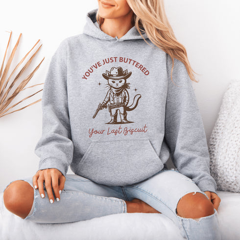 This hoodie is purr-fect for anyone who loves cats, chaos, and a healthy dose of cowboy attitude. Featuring a grumpy cat in a cowboy hat, pointing a tiny pistol