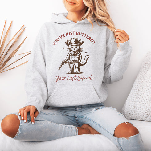 This hoodie is purr-fect for anyone who loves cats, chaos, and a healthy dose of cowboy attitude. Featuring a grumpy cat in a cowboy hat, pointing a tiny pistol