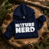 Navy hoodie with 'Nature Nerd' text on a wooden stump with pine cones and branches.