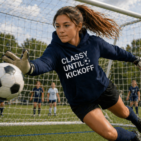 Female Soccer goalie wearing a “Classy Until Kickoff” hoodie standing on a soccer field during a youth soccer game