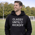 Man wearing “Classy Until Kickoff” hoodie standing on a soccer field during a youth soccer game