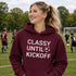 Woman wearing “Classy Until Kickoff” hoodie standing on a soccer field during a youth soccer game