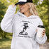 Woman wearing a Cleats On Game Face On soccer hoodie with player graphic, holding coffee outdoors