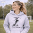 Woman wearing a Cleats On Game Face On soccer hoodie with player graphic, holding coffee outdoors