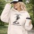 Woman wearing a Cleats On Game Face On soccer hoodie with player graphic, holding coffee outdoors