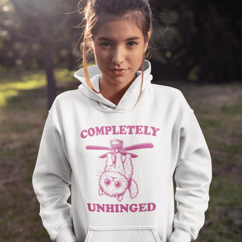This hoodie features a wildly unpredictable cat dangling upside-down from a ceiling fan, perfectly paired with the slogan "Completely Unhinged."