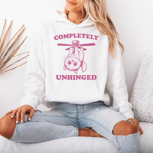 This hoodie features a wildly unpredictable cat dangling upside-down from a ceiling fan, perfectly paired with the slogan "Completely Unhinged."
