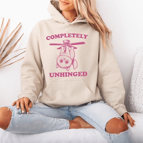This hoodie features a wildly unpredictable cat dangling upside-down from a ceiling fan, perfectly paired with the slogan "Completely Unhinged."