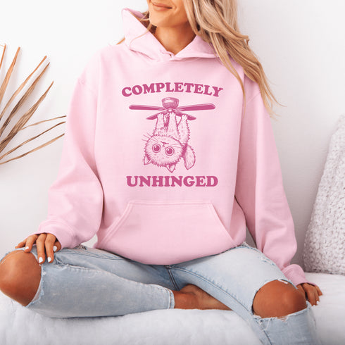 This hoodie features a wildly unpredictable cat dangling upside-down from a ceiling fan, perfectly paired with the slogan "Completely Unhinged."