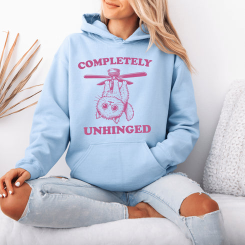 This hoodie features a wildly unpredictable cat dangling upside-down from a ceiling fan, perfectly paired with the slogan "Completely Unhinged."