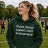Woman wearing a green hoodie with 'Crazy proud always loud soccer mom' text on a soccer field.