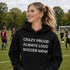 Woman wearing a black hoodie with 'Crazy proud always loud soccer mom' text on a soccer field.
