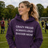 Woman wearing a purple hoodie with a soccer mom message on a soccer field.