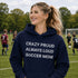 Woman wearing hoodie with "Crazy Proud Always Loud Soccer Mom" text standing on a soccer field during a youth soccer game