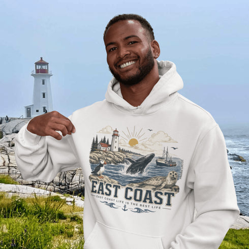 Man wearing a hoodie with a lighthouse and coastal design, standing in front of a lighthouse and ocean.