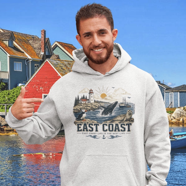 Person wearing East Coast Canada hoodie featuring lighthouse, ocean, and marine wildlife design in a coastal village setting