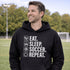 Man wearing a black “Eat Sleep Soccer Repeat” hoodie on a soccer field during a game, casual soccer apparel