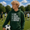 Teen wearing “Eat Sleep Soccer Repeat” hoodie holding a soccer ball on a soccer field during a game, casual soccer apparel